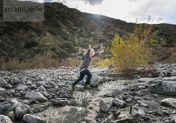 Junge springt im Flussbett über Felsen