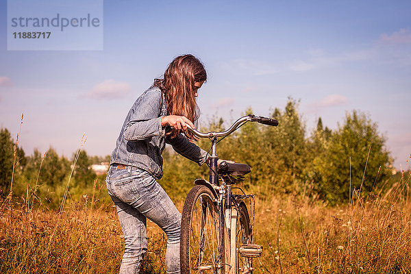 Teenager-Mädchen lehnt sich an und besteigt ihr Fahrrad auf dem Feld