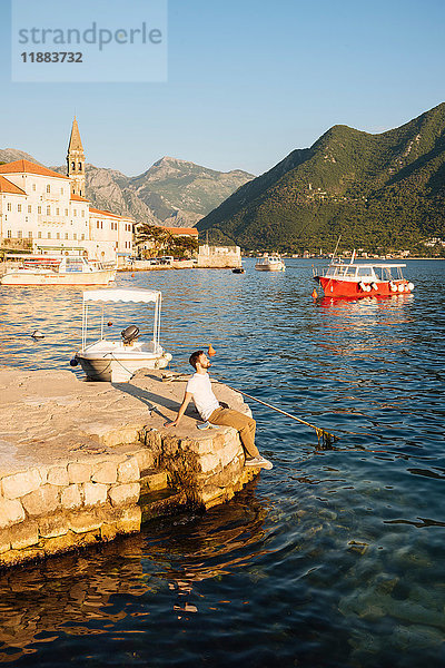 Mann sitzt auf der Mole im Hafen und schaut weg  Perast  Montenegro  Europa