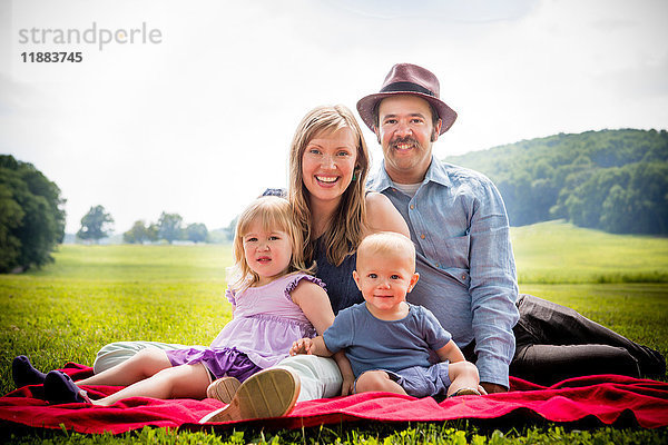 Porträt eines Ehepaares mittlerer Erwachsener auf einer Picknickdecke sitzend mit Tochter und kleinem Sohn