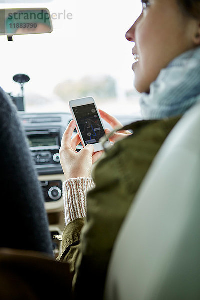 Junges Paar sitzt im Auto  Frau hält Smartphone  Rückansicht