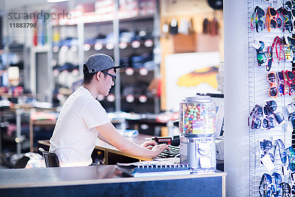 Junger männlicher Verkaufsassistent tippt an der Computertastatur an der Theke eines Skateboard-Ladens