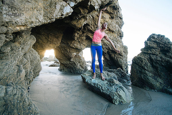 Junge Frau steht auf Felsen am Strand  macht Sport  dehnt sich