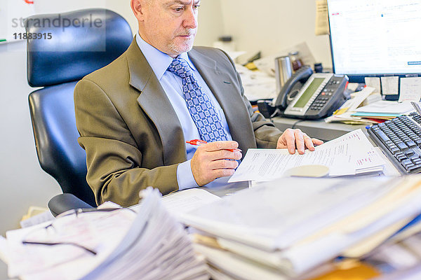 Geschäftsmann liest Papierkram am Büroschreibtisch