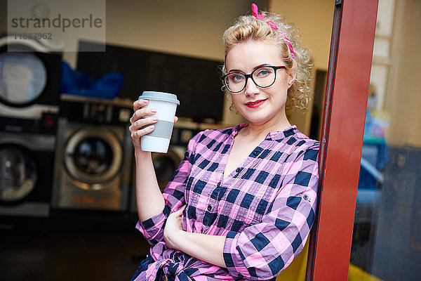 Porträt einer schrulligen Frau  die sich an die Tür eines Waschsalons lehnt