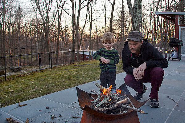 Junge und Vater hüten Feuer in der Feuergrube im Innenhof