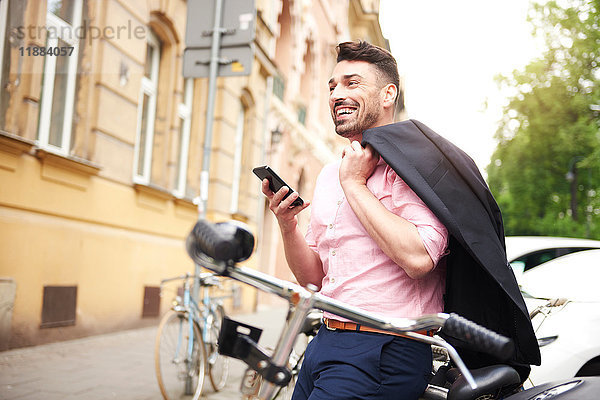 Mann mit Fahrrad hält Smartphone lächelnd in der Hand