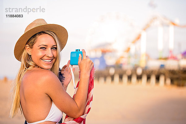 Porträt einer jungen Frau in Bikini-Oberteil beim Fotografieren eines Vergnügungsparks am Strand  Santa Monica  Kalifornien  USA