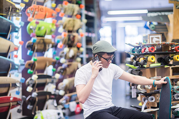 Junger männlicher Skateboarder telefoniert mit seinem Smartphone im Skateboard-Shop