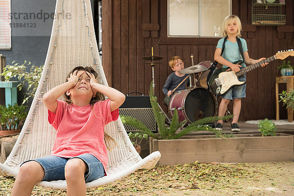 Mädchen im Hängestuhl  Hände auf dem Kopf und Kinder  die in einer Band Gitarre und Schlagzeug spielen