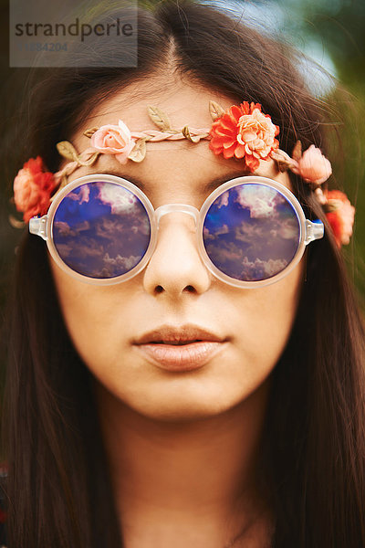 Porträt einer jungen Hippiefrau mit Blumenstirnband und Sonnenbrille beim Festival