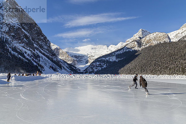 Touristen genießen das Schlittschuhlaufen auf dem zugefrorenen See an einem sonnigen Tag mit dieser malerischen Aussicht auf die Berge; Lake Louise  Alberta  Kanada'.