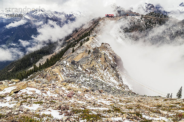 Auf dem Gipfel des Wanderwegs auf dem Kicking Horse Mountain sind in der Ferne in den Wolken die Gondel und die Skihütte zu sehen  die für die Rückwanderung vorgesehen sind. Kicking Horse Mountain Resort im Sommer; Golden  British Columbia  Kanada.