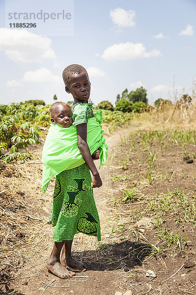 Ein junges Mädchen trägt ein Baby in einem Tragetuch auf dem Rücken; Uganda .