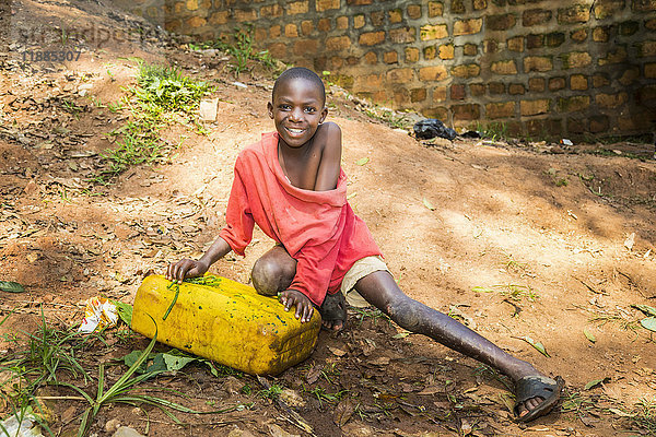 Ein kleiner Junge lächelt in die Kamera  während er auf dem Boden hockt; Uganda