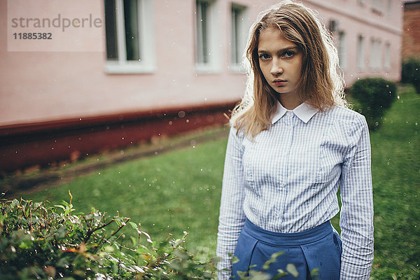Porträt eines jungen Mädchens  das bei Pflanzen gegen das Bauen im Regen steht.