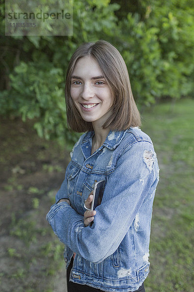 Porträt einer lächelnden jungen Frau mit gekreuzten Armen im Park stehend