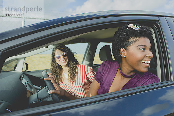 Lächelnde junge Frau schaut weg  während sie mit einer Freundin im Auto sitzt.