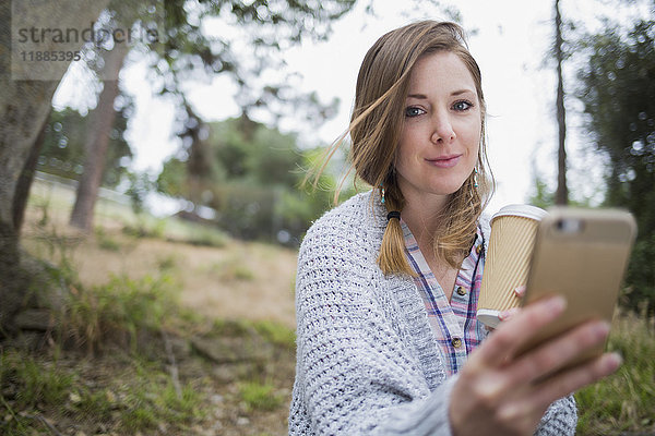 Porträt einer schönen Frau mit Einwegglas und Smartphone im Park
