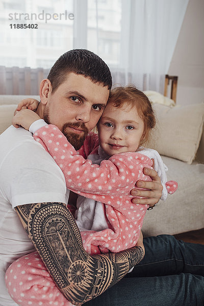 Porträt eines lächelnden Vaters und einer lächelnden Tochter  die sich auf dem Sofa zu Hause umarmen.