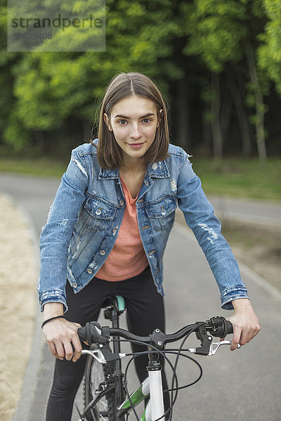 Porträt einer lächelnden Frau beim Radfahren auf der Straße im Park