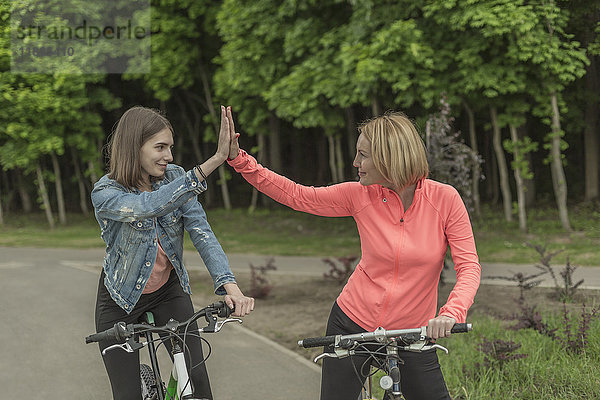 Lächelnde Mutter und Tochter  die beim Radfahren im Park high-five machen