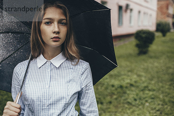 Porträt eines Teenagermädchens mit Regenschirm auf grasbewachsenem Feld