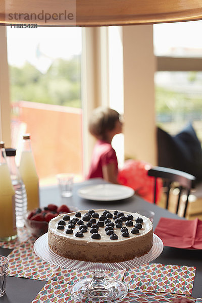 Torte auf Standmatten am Esstisch mit spielendem Mädchen im Hintergrund