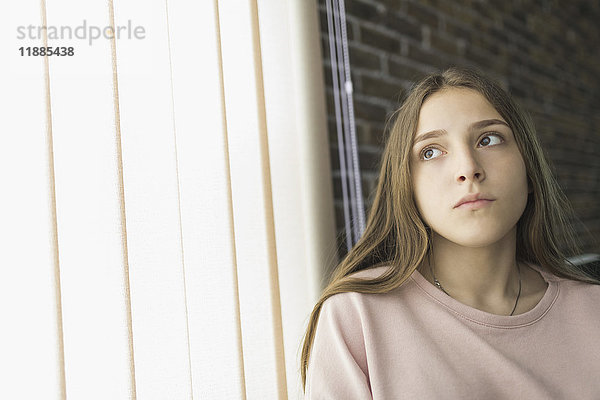 Teenager-Mädchen am Vorhang zu Hause sitzend