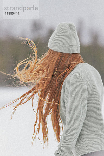 Junge Frau mit langen roten Haaren mit Strickmütze und Pullover gegen den klaren Himmel