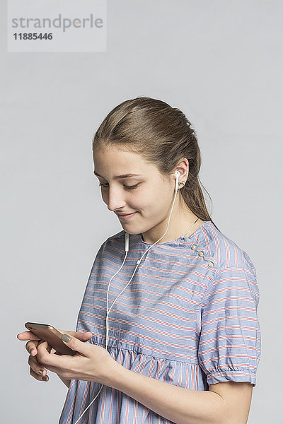 Lächelndes Mädchen beim Musikhören mit dem Handy vor weißem Hintergrund