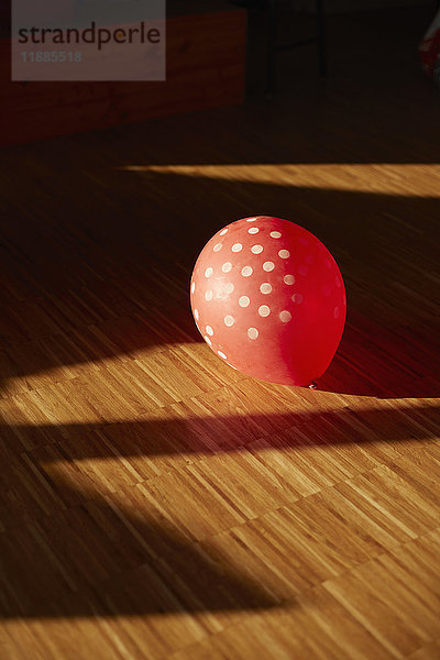 Hochwinkelansicht des gefleckten roten Ballons auf Hartholzboden im Sonnenlicht zu Hause