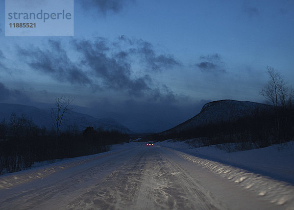 Fernansicht des Autos auf schneebedeckter Straße gegen den Himmel in der Dämmerung  Kiruna  Schweden