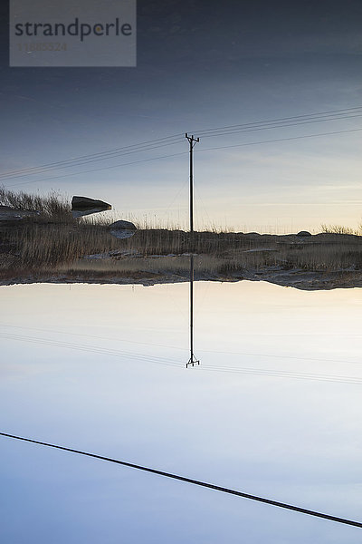 Strommast reflektiert im ruhigen See gegen den blauen Himmel