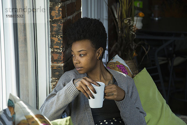 Junge Frau mit Kaffee und Blick durchs Fenster zu Hause