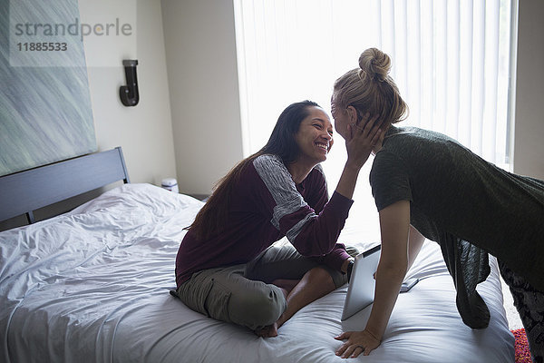 Lächelndes junges lesbisches Paar im Bett mit digitalem Tablett zu Hause