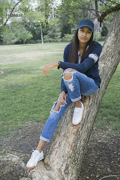 Porträt einer jungen Frau  die auf einem Baumstamm im Park sitzt.