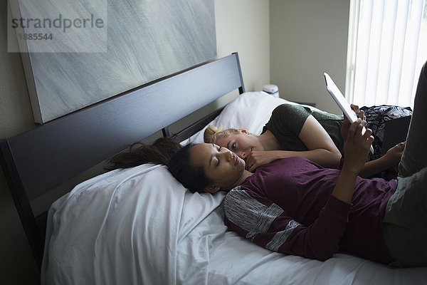 Hochwinkelansicht einer Frau  die ihre Freundin mit einem digitalen Tablett betrachtet  während sie zu Hause auf dem Bett liegt.