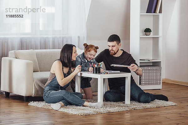 Glückliche Eltern malen mit Tochter im Wohnzimmer zu Hause