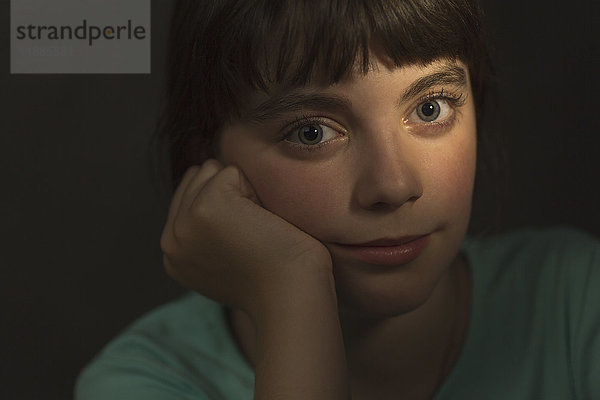 Porträt eines Mädchens  das mit der Hand auf dem Kinn auf grauem Hintergrund ruht.