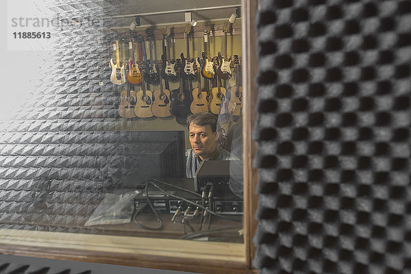 Musiker mit Computer vom Fensterglas aus gesehen im Aufnahmestudio
