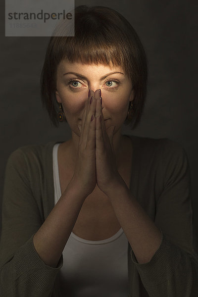 Mittlere erwachsene Frau meditiert mit den Händen vor grauem Hintergrund.