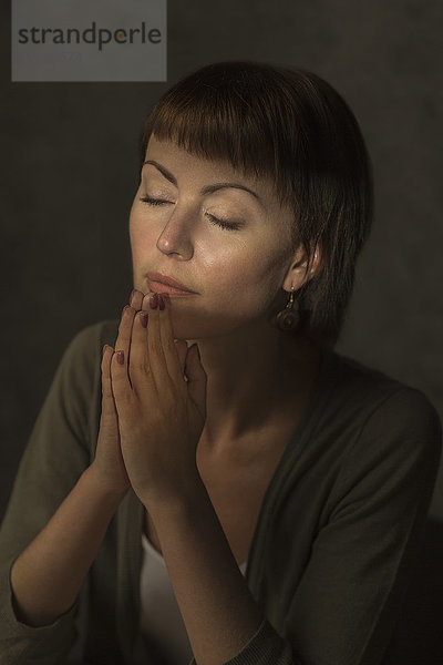 Mittlere erwachsene Frau mit geschlossenen Augen  die vor grauem Hintergrund betet.