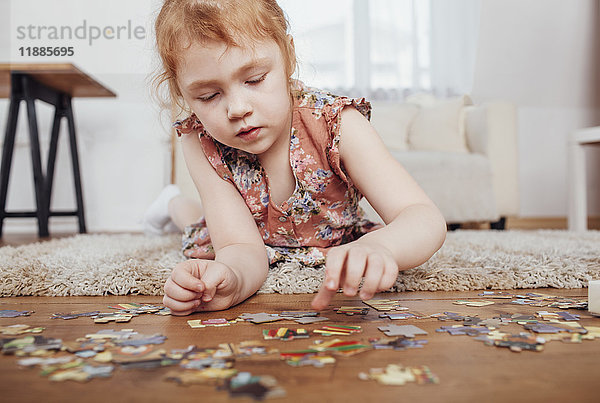 Mädchen spielt mit Puzzleteilen  während sie zu Hause auf dem Teppich liegt.