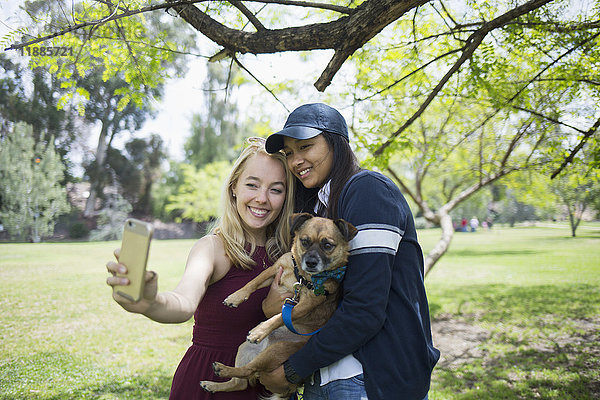 Lächelnde junge Frauen  die Selfie mit Hund im Park mitnehmen.
