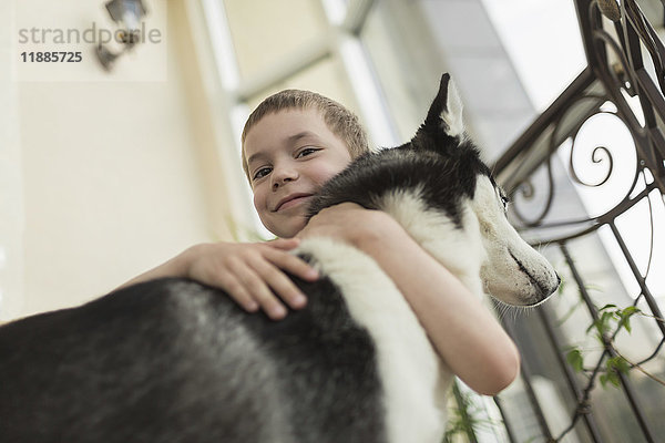 Niederwinkel-Porträt eines Jungen  der den Hund mit einem Geländer umarmt.