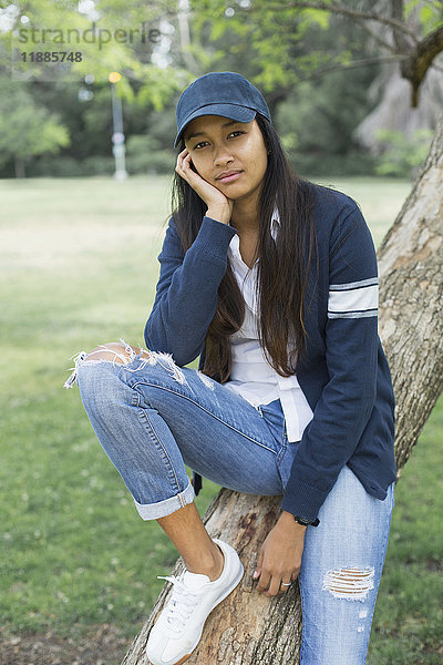 Porträt einer jungen Frau  die auf einem Baumstamm im Park sitzt.