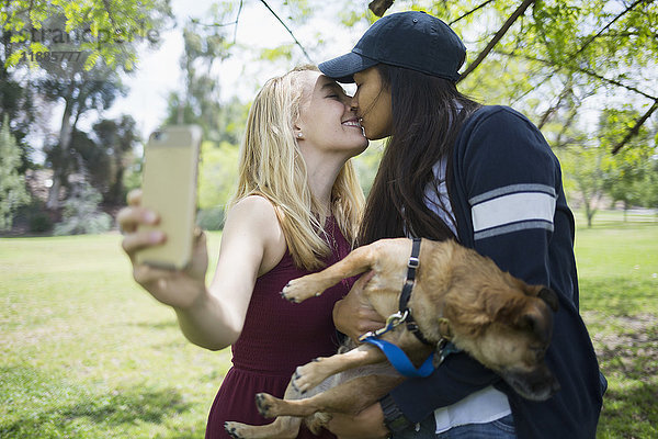 Frau  die sich küsst  während sie Selfie mit Hund im Park nimmt.