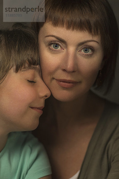 Porträt der lächelnden Mutter mit liebevoller Tochter vor grauem Hintergrund