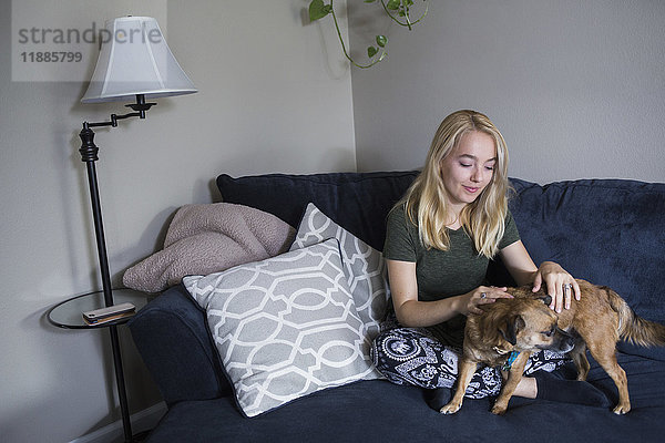 Junge blonde Frau sitzend mit Hund auf dem Sofa zu Hause